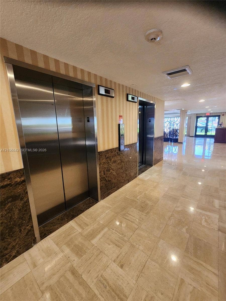 Lobby featuring dual stainless steel elevators, polished stone tile flooring, and decorative stone wainscoting