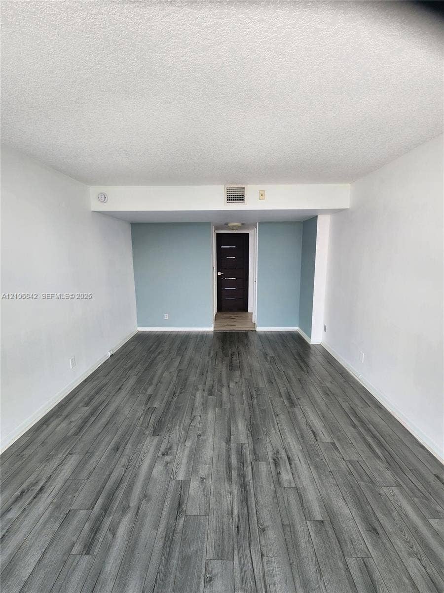 Interior room featuring wood-finish flooring, textured ceiling, and a dark-toned door with horizontal panel detailing