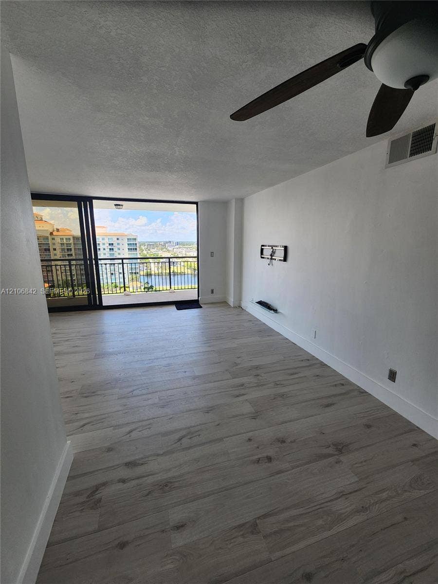 Interior space featuring wood-finish flooring, ceiling fan, and sliding glass doors leading to a balcony with water and building scenery