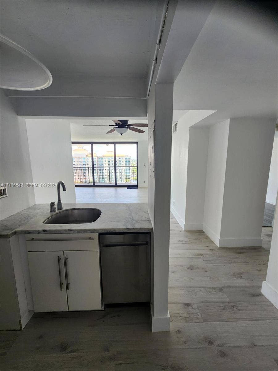 Kitchenette featuring stone-finish countertops, stainless steel sink, under-counter stainless steel dishwasher, and wood-finish flooring