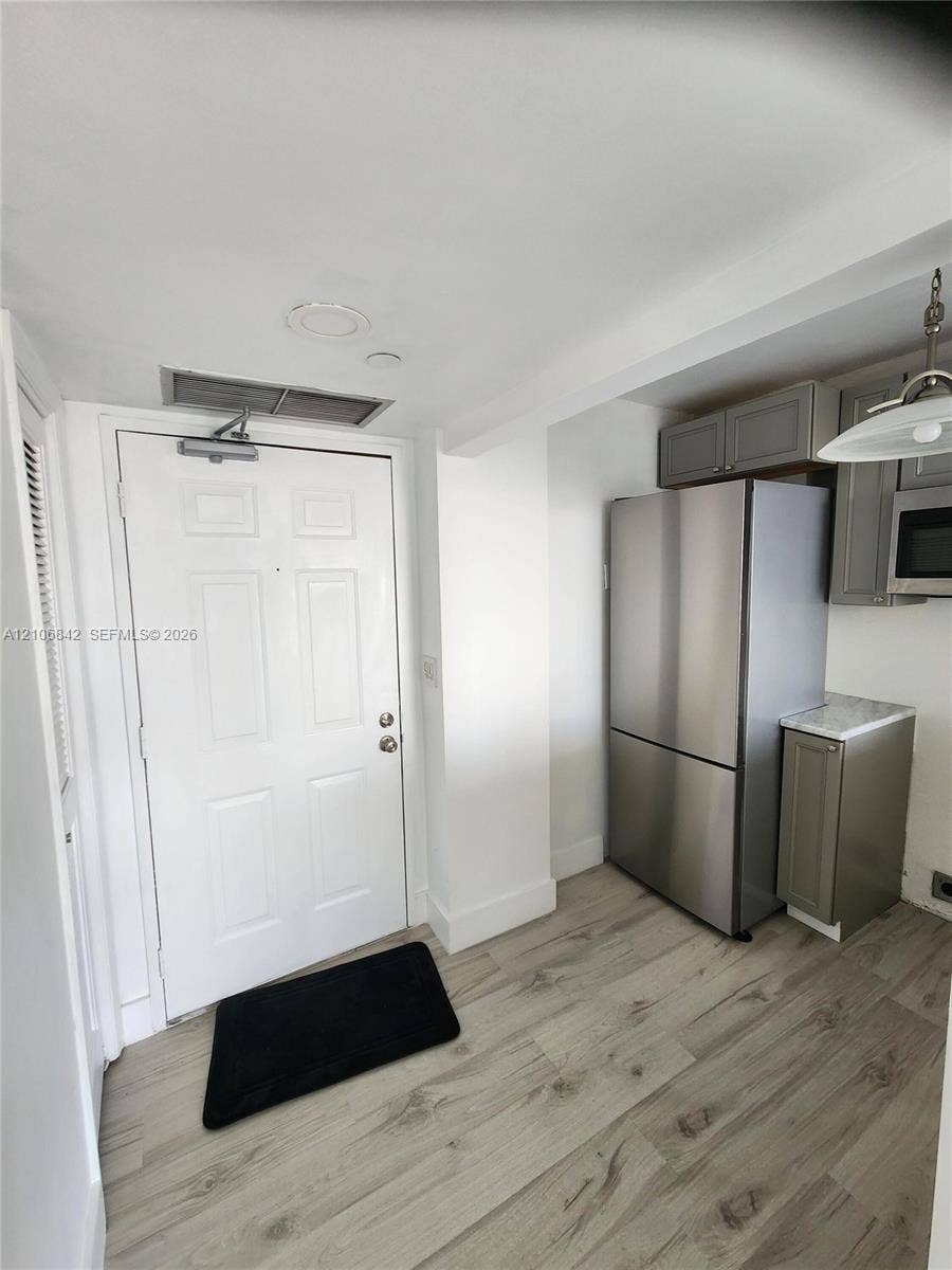 Kitchen featuring wood-finish flooring, stainless steel refrigerator, grey cabinetry, and stone-finish countertops