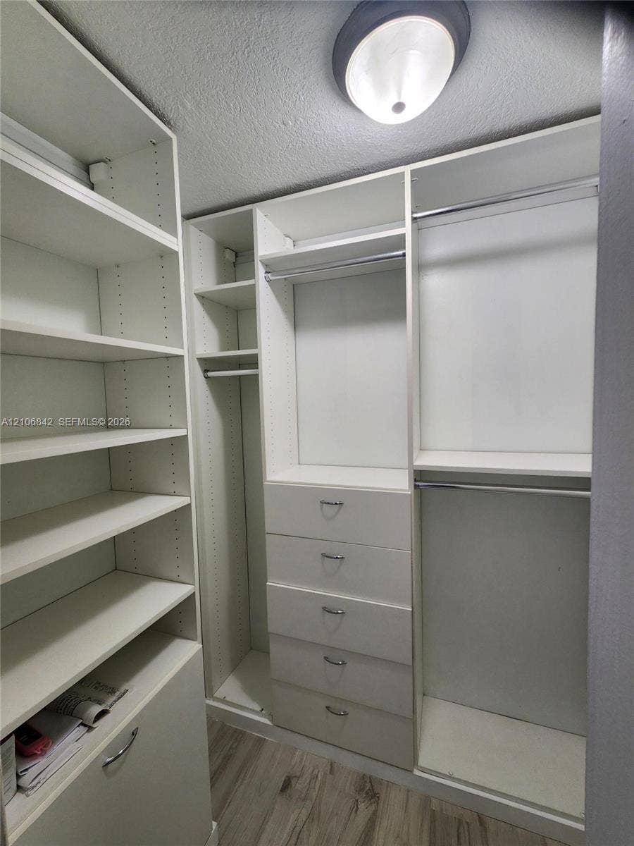 Custom built-in storage system featuring floor-to-ceiling shelving, integrated drawers with metallic pulls, dual hanging rods, and wood-finish flooring