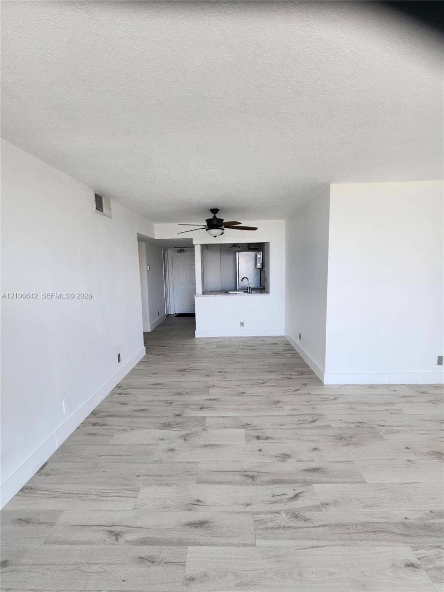 Wood-finish flooring throughout, ceiling-mounted fan, and kitchen pass-through window with a peninsula counter