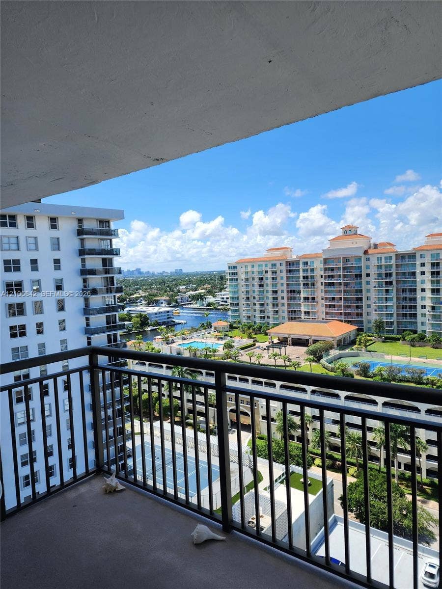 Private balcony with metal railing, overlooking urban buildings, a swimming pool, and a tennis court