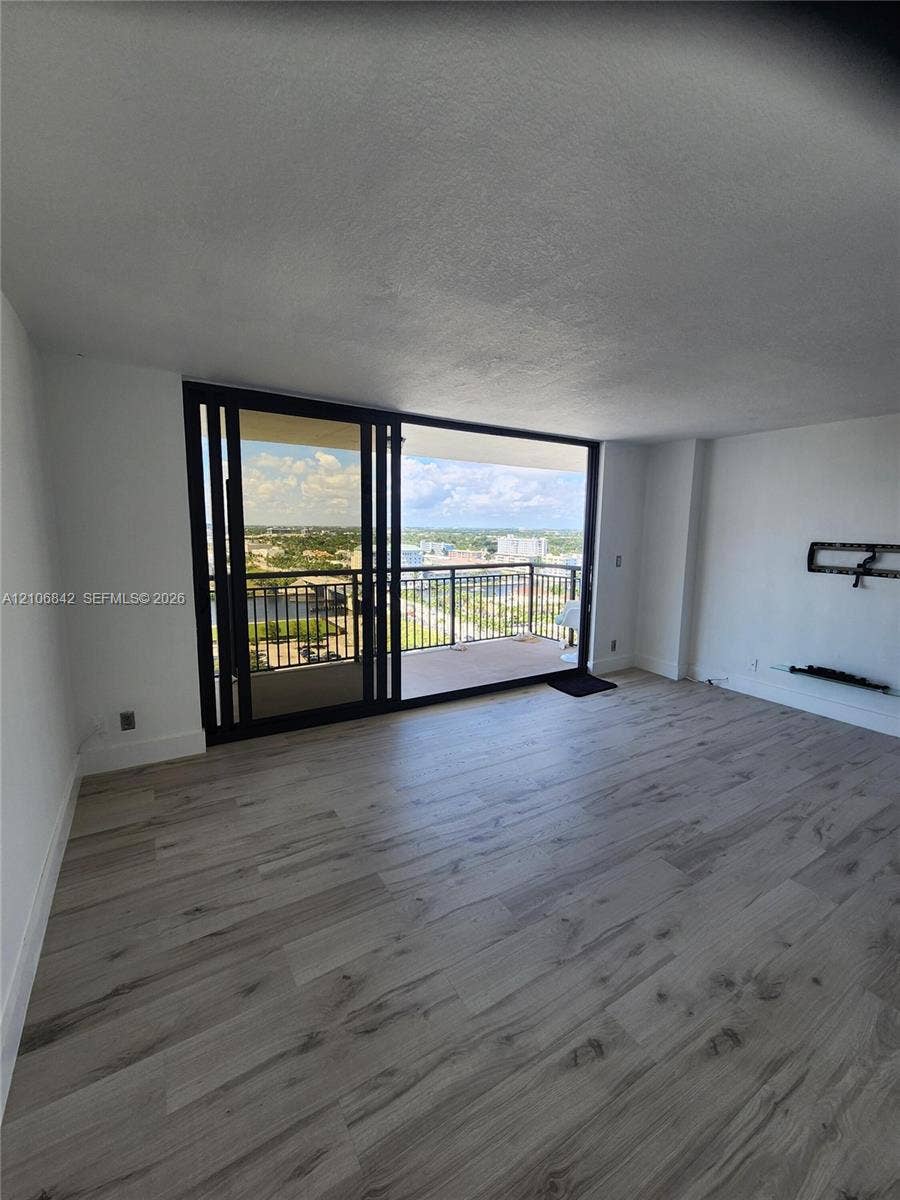 Living area featuring wood-finish flooring, floor-to-ceiling sliding glass doors, and a private balcony with metal railings
