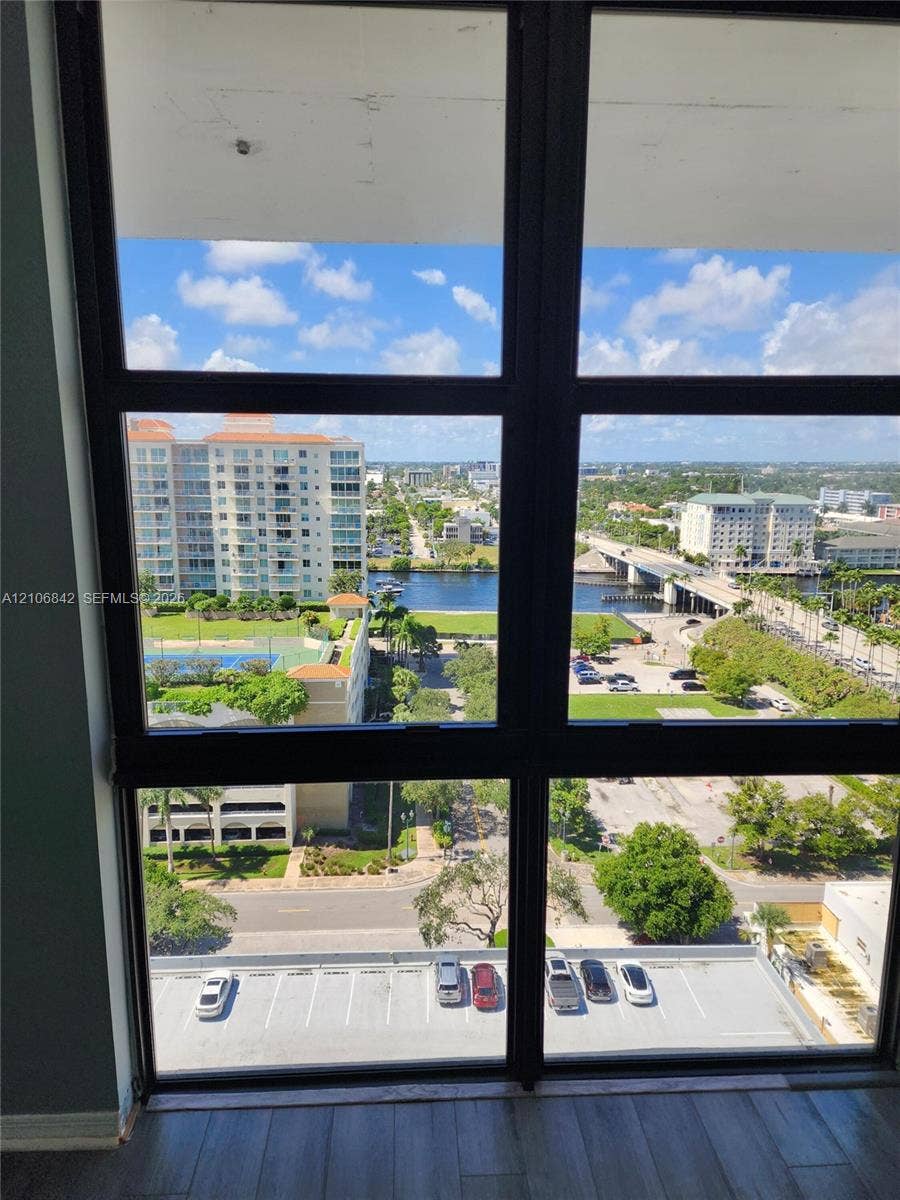 Floor-to-ceiling windows featuring black framing, showcasing expansive exterior sights including a waterfront, multi-story urban buildings, and surrounding landscaping