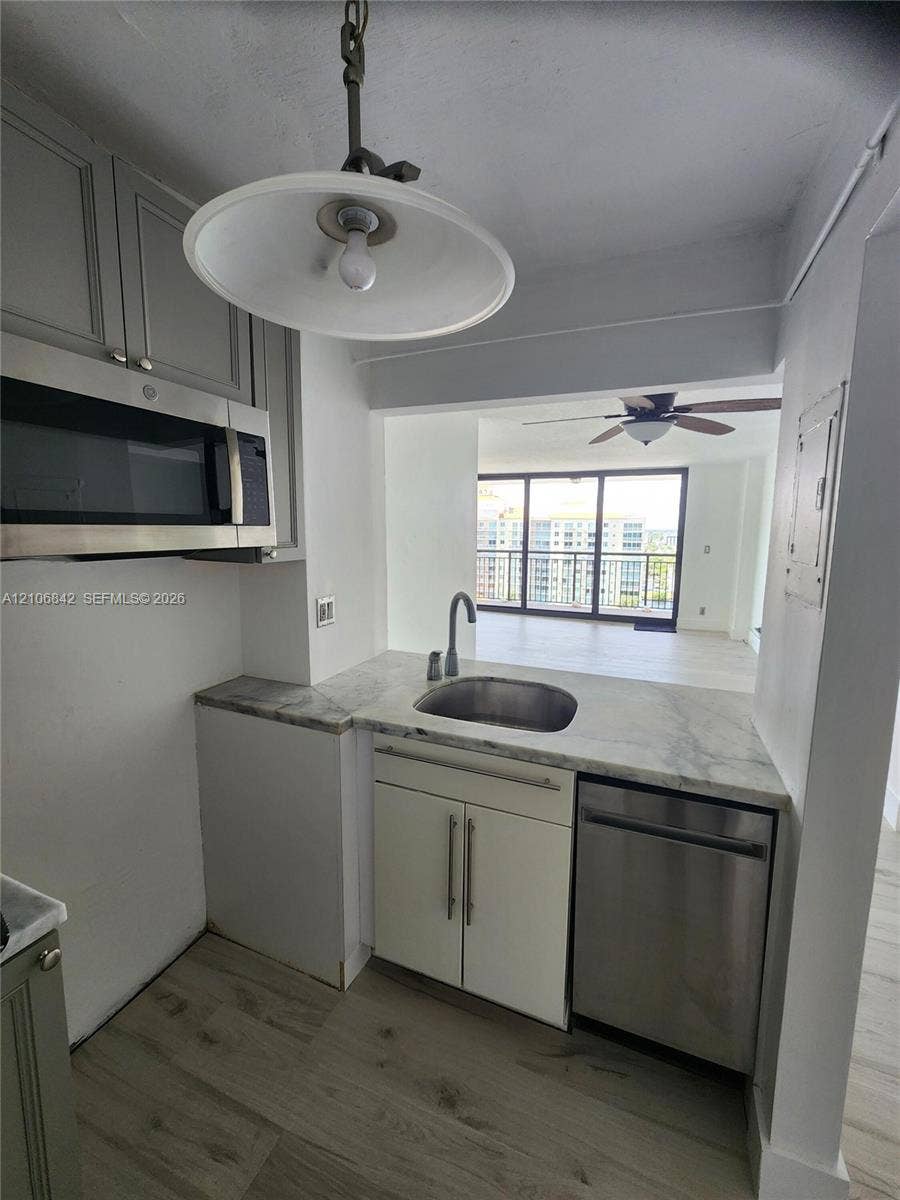 Kitchen area featuring light-toned cabinetry, stainless steel appliances, stone-finish countertops, an undermount sink with a gooseneck faucet, and wood-finish flooring