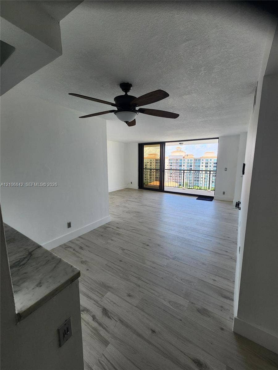 Light-toned wood-finish flooring, stone-surfaced counter, ceiling fan with integrated lighting, and full-height sliding glass doors leading to a balcony
