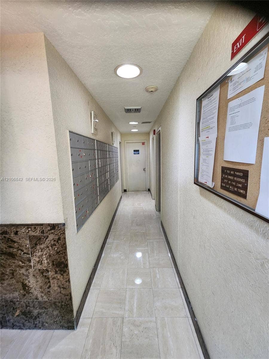 Interior corridor featuring stone-finish floor tiling, wall-mounted mail lockers, recessed lighting, and decorative stone-textured wall accents