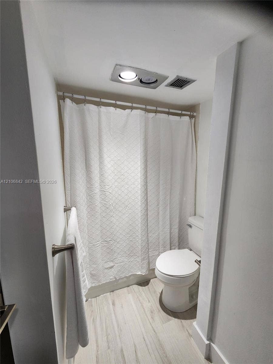 Bathroom featuring wood-finish flooring, a wall-mounted brushed nickel towel bar, and a recessed ceiling light fixture