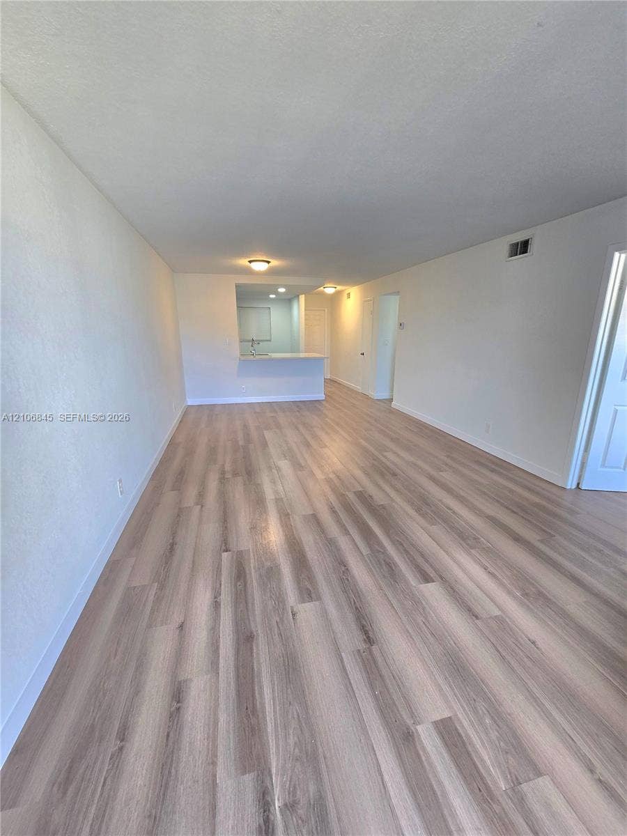 1700 NW 58th Terrace, #3J, Sunrise, Sunrise, FL 33313 Open-concept interior featuring light-toned wood-finish flooring, neutral walls, flush-mount ceiling lighting, and a kitchen pass-through counter