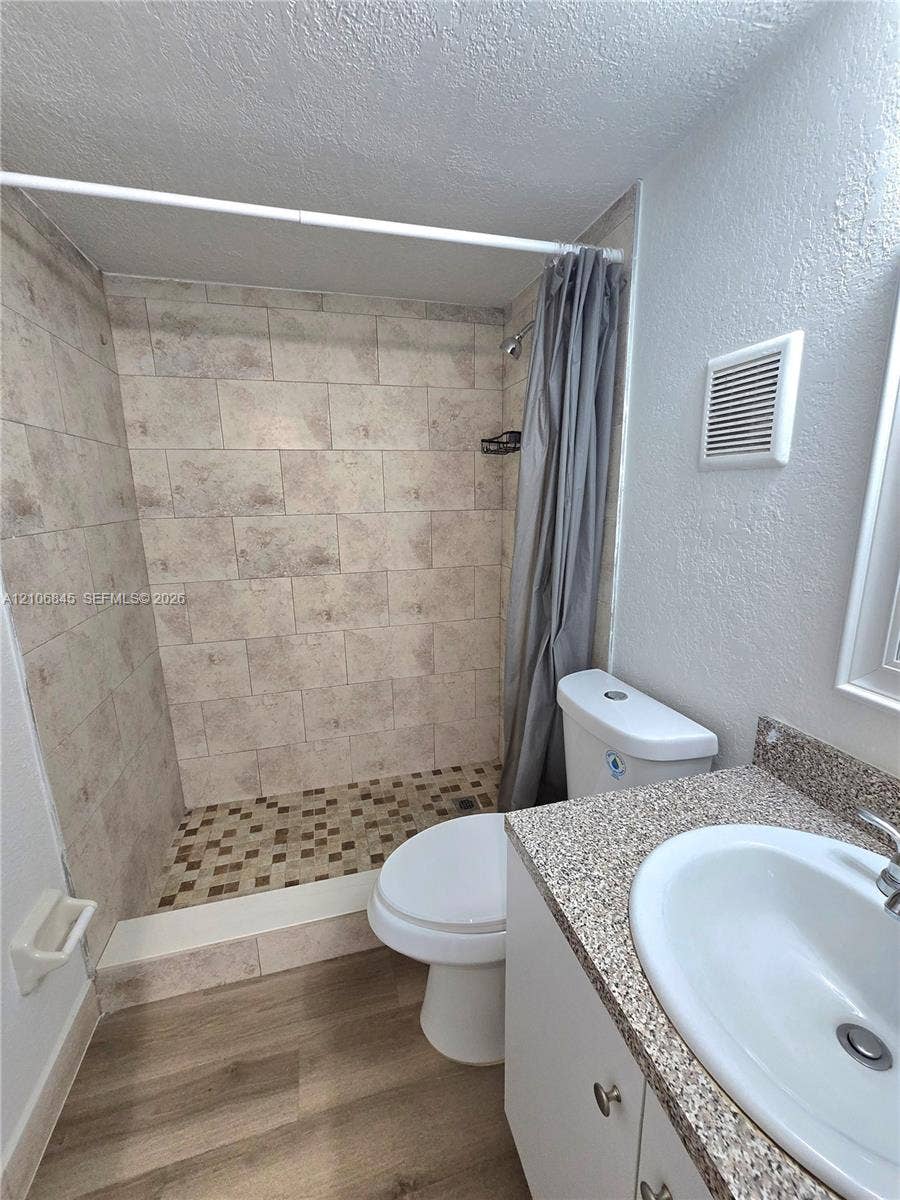 1700 NW 58th Terrace, #3J, Sunrise, Sunrise, FL 33313 Bathroom featuring a walk-in shower with tile surround, mosaic tile flooring, vanity with stone-finish countertop, integrated sink, and wood-finish flooring