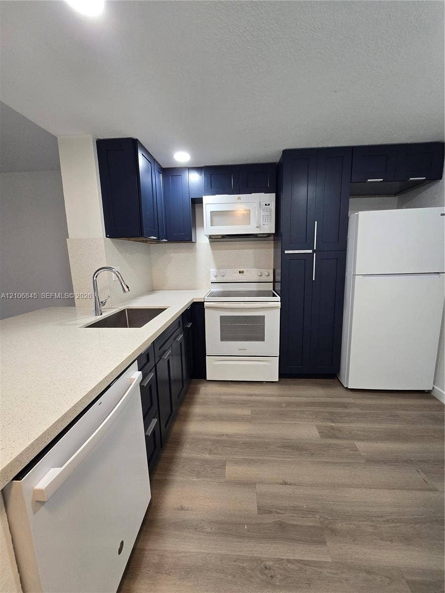 1700 NW 58th Terrace, #3J, Sunrise, Sunrise, FL 33313 Kitchen featuring navy cabinetry, solid-surface countertops, wood-finish flooring, stainless steel sink with high-arch faucet, and white appliances