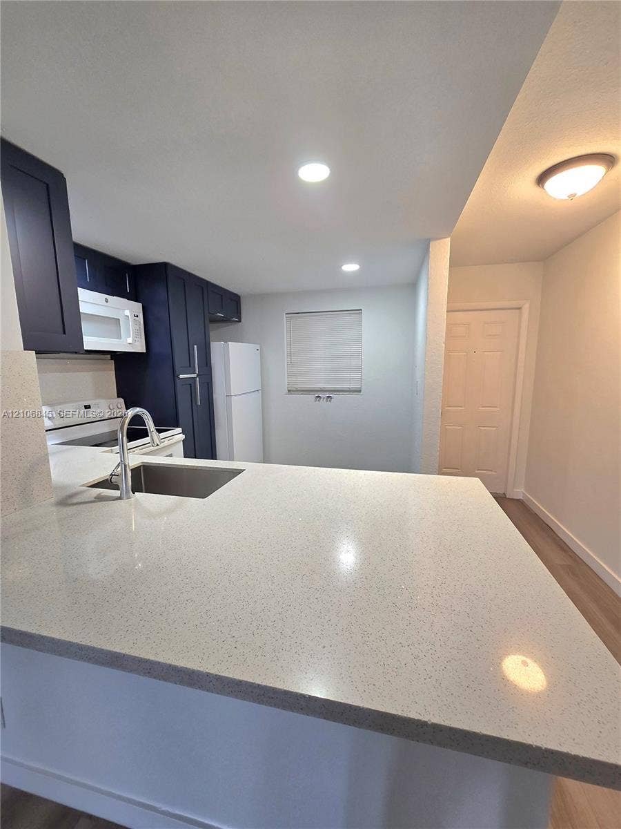 1700 NW 58th Terrace, #3J, Sunrise, Sunrise, FL 33313 Kitchen featuring navy blue cabinetry, light-toned stone-finish countertops, stainless steel undermount sink with arched faucet, recessed lighting, and wood-finish flooring