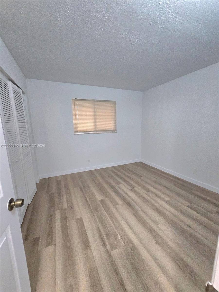 1700 NW 58th Terrace, #3J, Sunrise, Sunrise, FL 33313 Neutral-toned wood-finish flooring, white walls, and a built-in closet with louvered doors