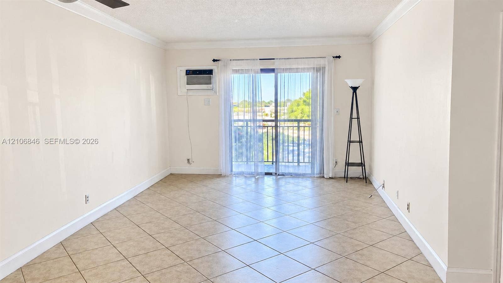 Interior space featuring tile flooring laid on a diagonal, crown molding, a built-in wall-mounted cooling unit, and a sliding glass door providing access to a railed balcony