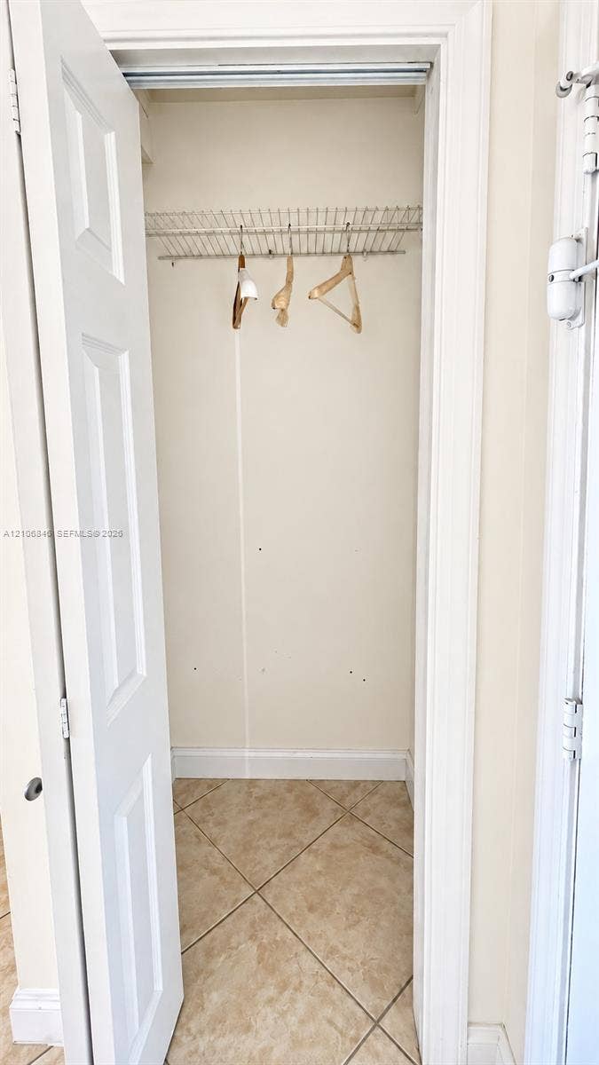 Reach-in closet featuring a hinged panel door, integrated wire shelving, and neutral tile flooring