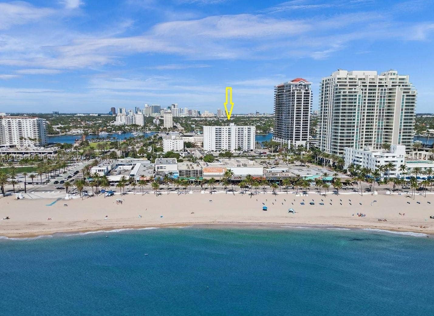 Aerial perspective of a high-rise residential structure positioned on the coast, featuring direct proximity to the shoreline, sand beach, and maritime surroundings