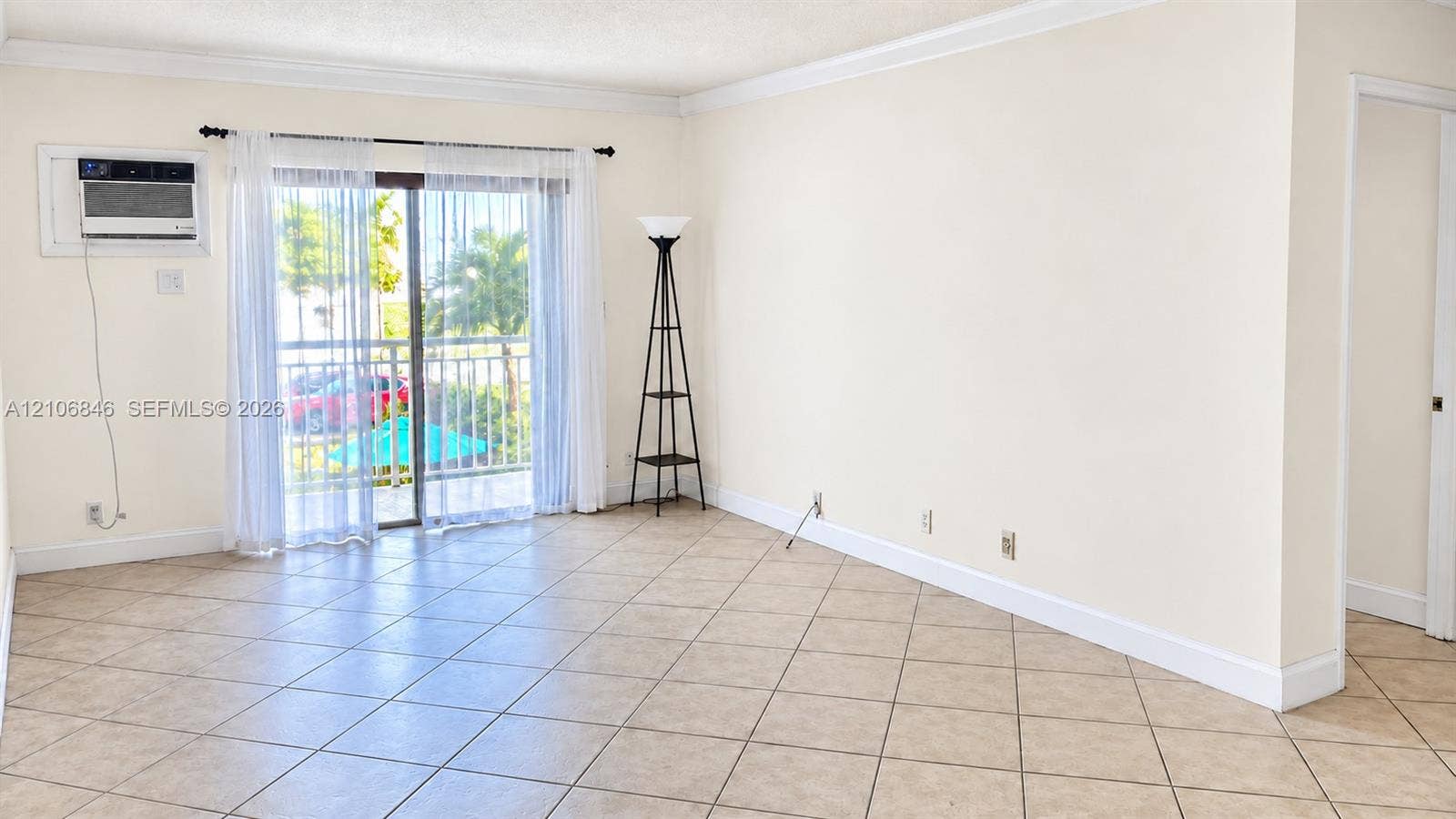 Neutral-toned interior featuring ceramic tile flooring, crown molding, and sliding glass doors with balcony access