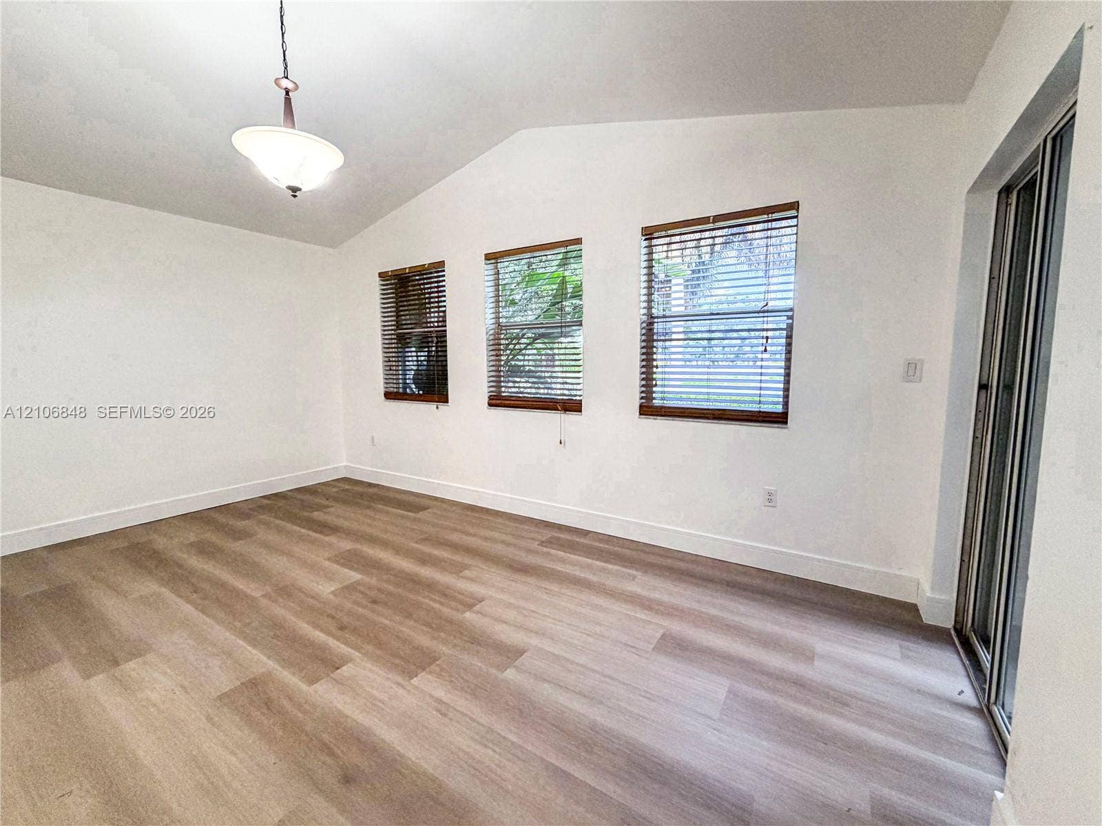 Vaulted ceilings, wood-finish flooring, three windows with horizontal blinds, and sliding glass door