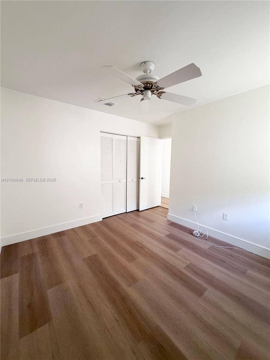 Interior room featuring wood-finish flooring, white walls, louvered closet doors, and a ceiling fan with integrated lighting