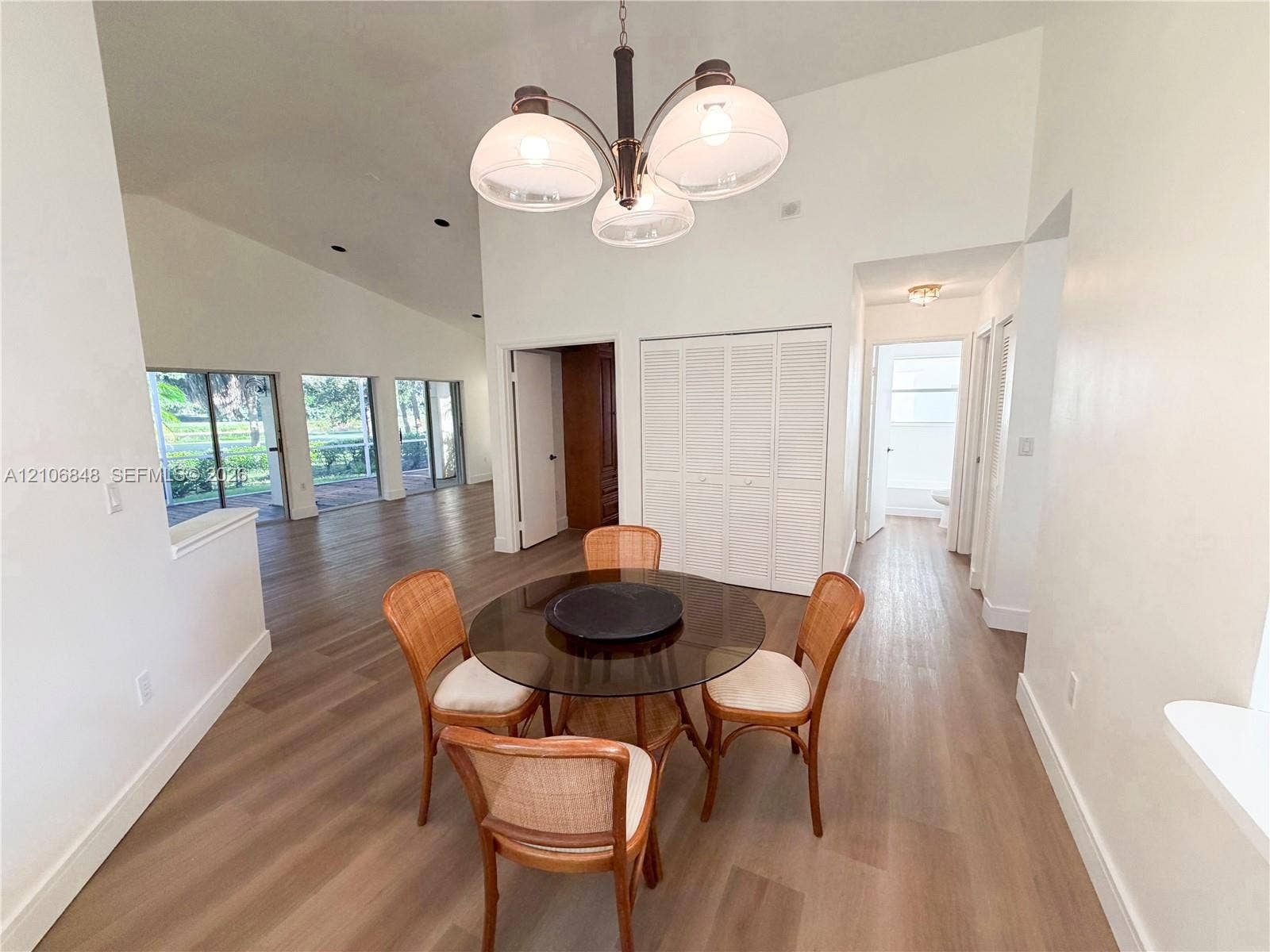 Vaulted ceilings, wood-finish flooring, multi-panel glass doors, recessed lighting, and a multi-globe chandelier