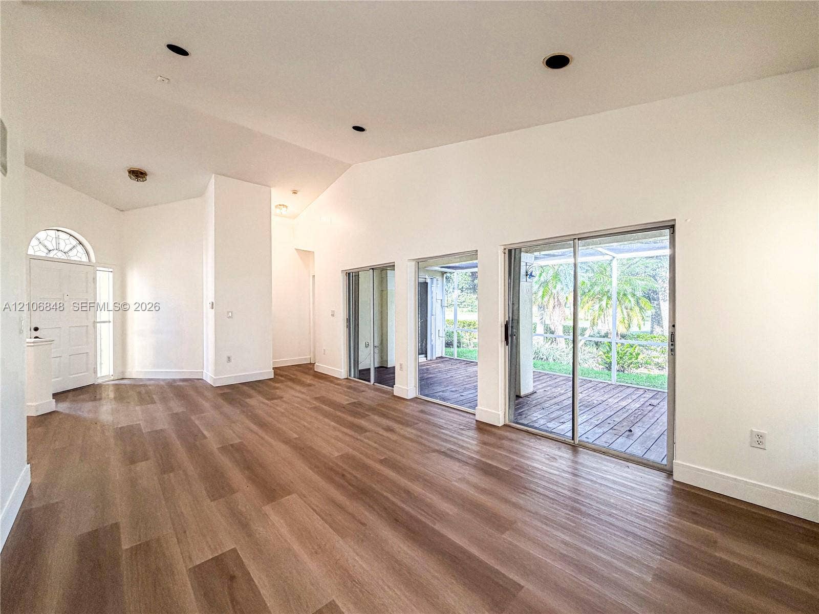 Vaulted ceilings, wood-finish flooring, recessed lighting, arched entry door with decorative glass, and triple glass sliding doors opening to a screened-in lanai