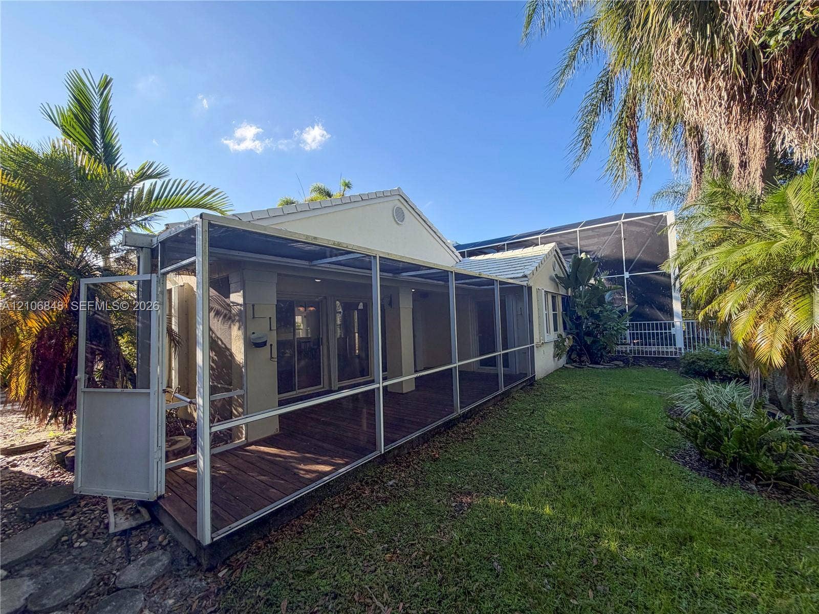 Screened-in lanai featuring wood-finish decking, aluminum framing, and sliding glass door access to the exterior, set against a manicured lawn with mature landscaping