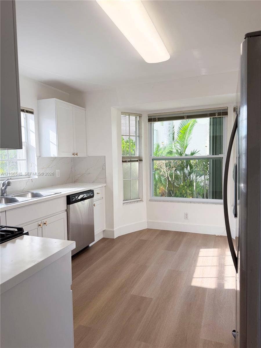 Kitchen featuring white shaker cabinetry, stone-finish countertops, full-height stone-finish backsplash, stainless steel appliances, and wood-finish flooring