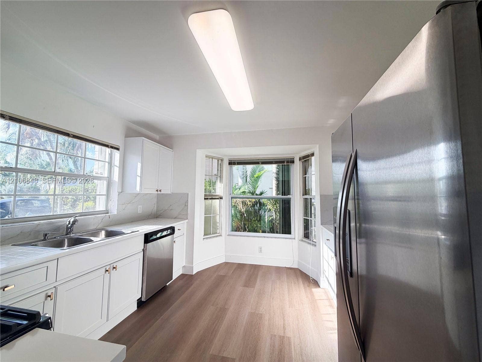 Kitchen featuring wood-finish flooring, white cabinetry, stainless steel appliances, a double-basin sink, and a bay window