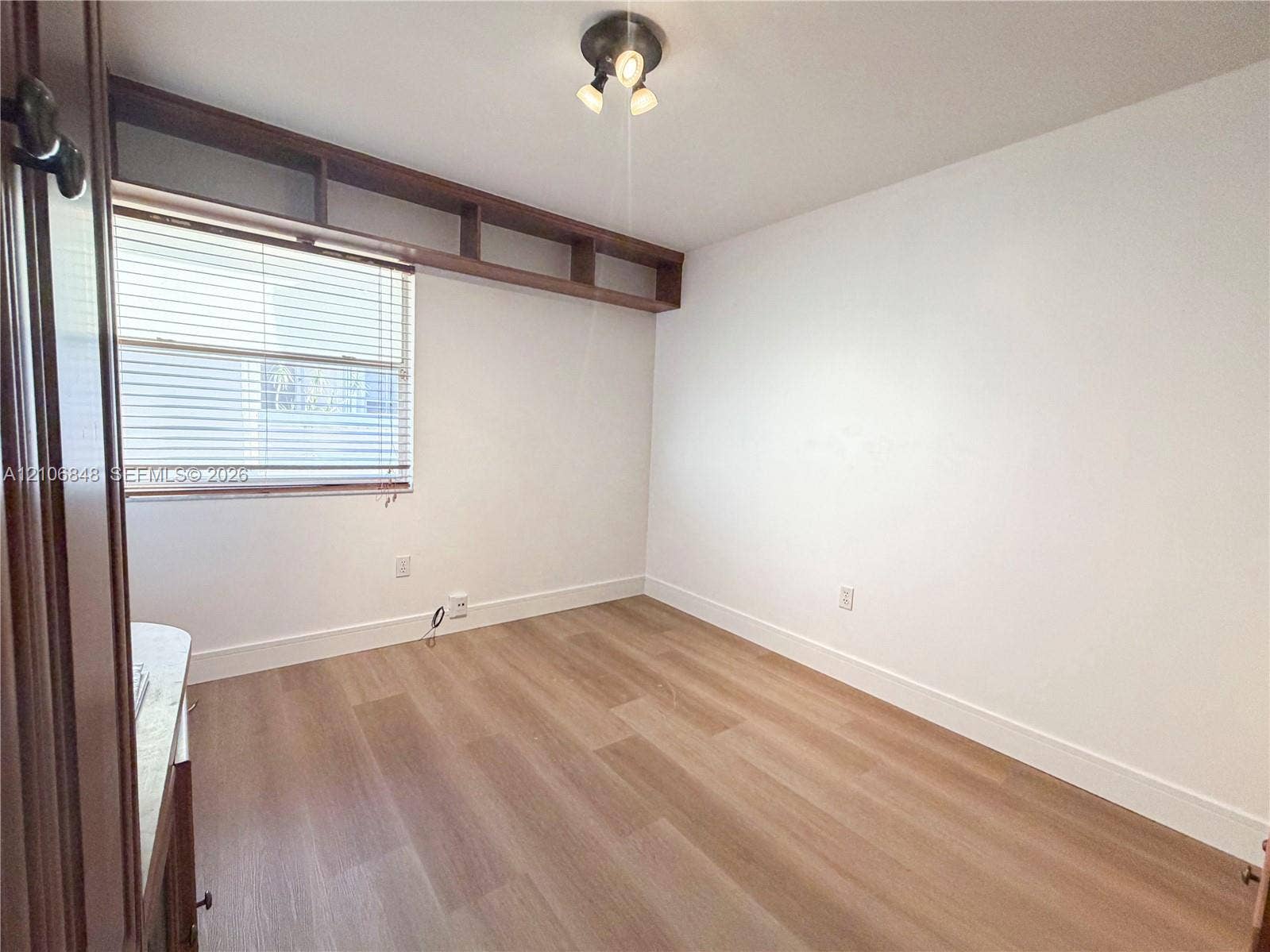 Interior space featuring wood-finish flooring, built-in wooden shelving above a window, and flush-mount ceiling lighting