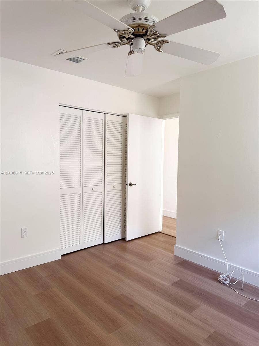 Wood-finish flooring, white louvered closet doors, and ceiling fan with integrated light fixture