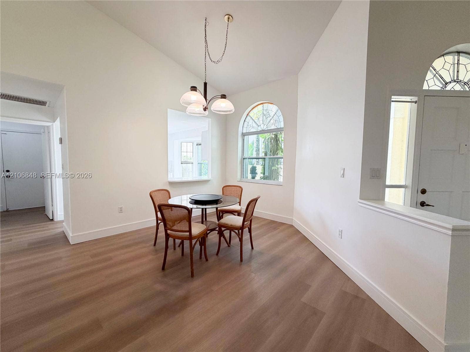 Vaulted ceilings, wood-finish flooring, arched window, and three-globe pendant lighting fixture