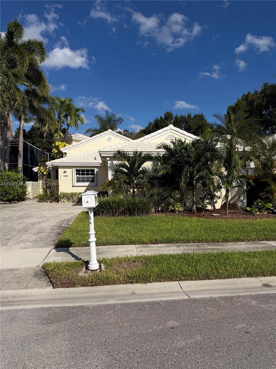 Single-story exterior featuring a light-toned stucco faade, dual-gabled roofline, paver driveway, and established palm landscaping
