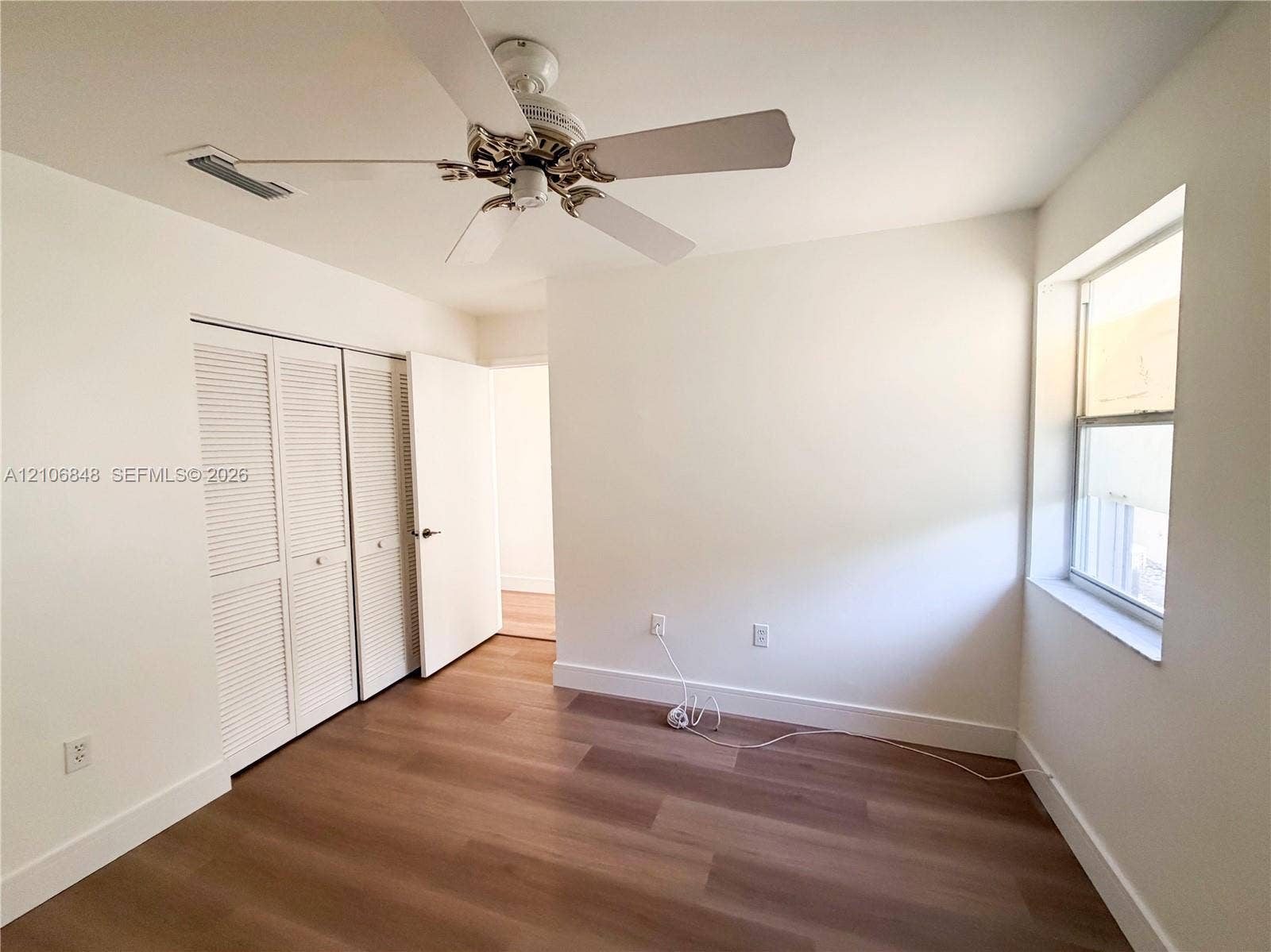 Room featuring wood-finish flooring, dual-panel louvered closet doors, and a ceiling-mounted fan