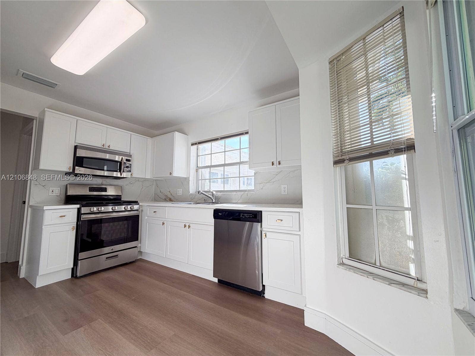 Kitchen featuring white shaker-style cabinetry, stone-patterned backsplash, stainless steel appliances, and wood-finish flooring