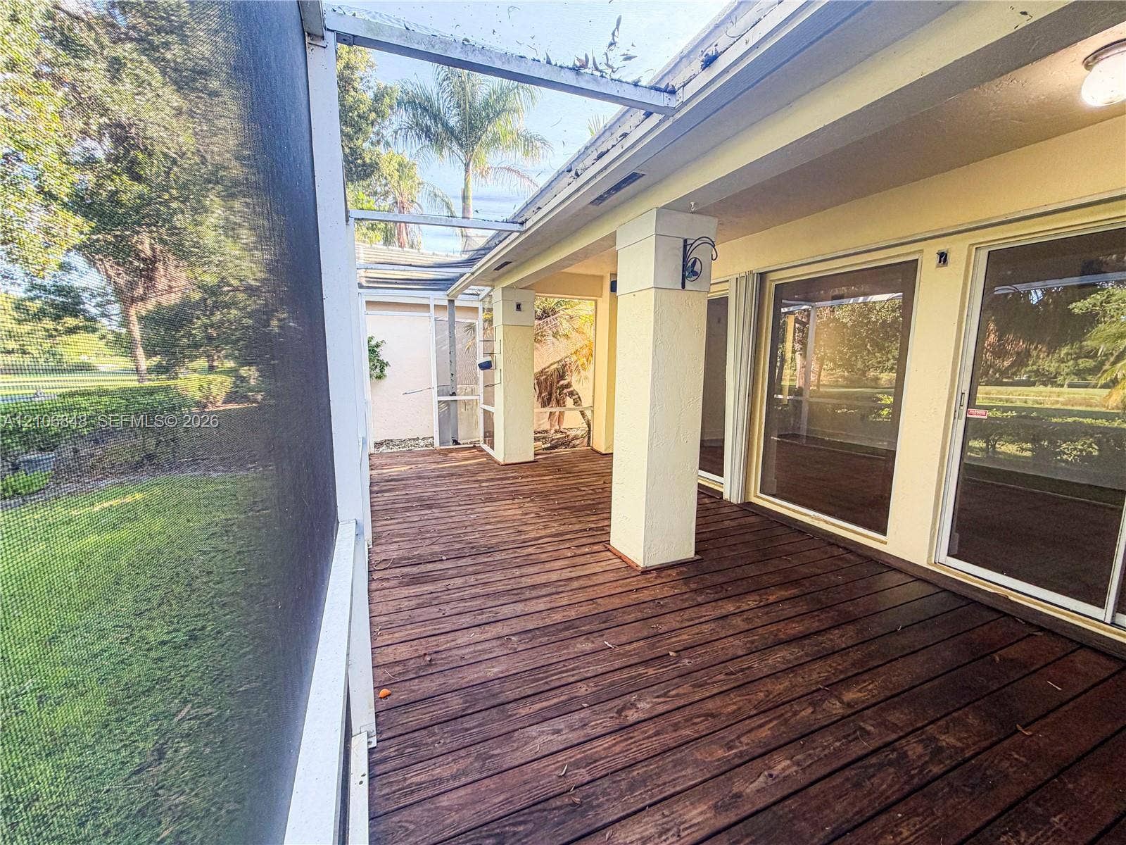 Screened-in porch featuring wood-finish decking, structural support pillars, and glass sliding door access