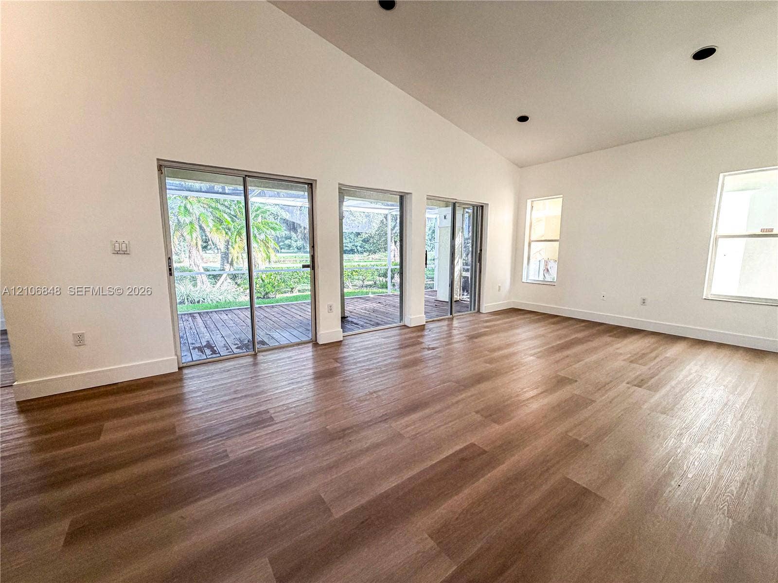 Vaulted ceilings, wood-finish flooring, recessed lighting, and multiple sliding glass doors providing outdoor access