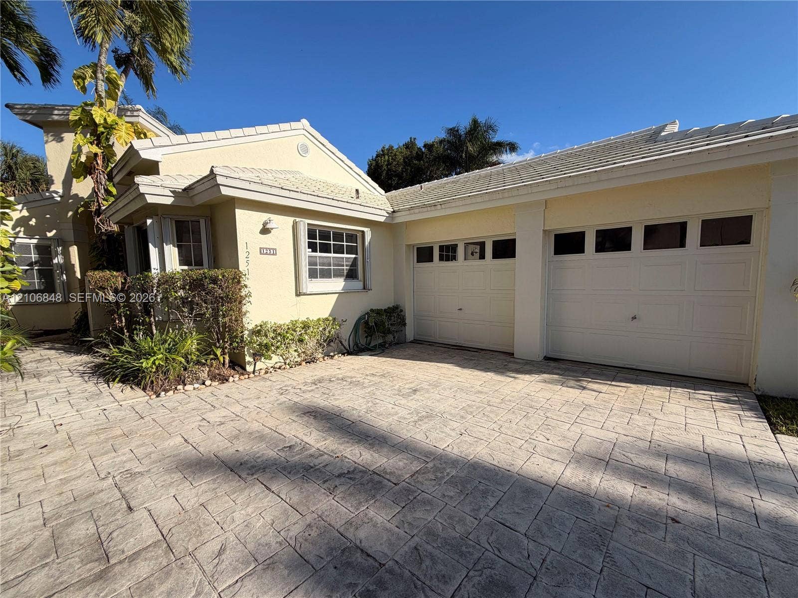 Stucco exterior with a tiled roof, paver driveway, and a two-car garage featuring paneled doors with window inserts