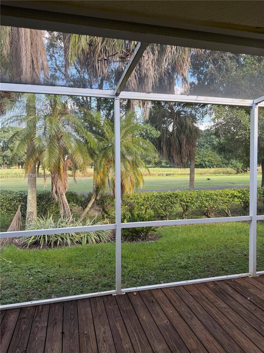 Screened-in enclosure featuring a wood-plank deck and mature palm trees