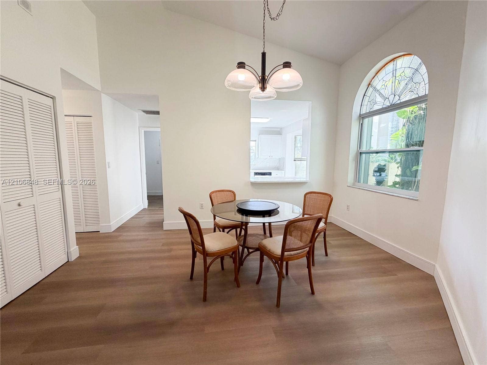 Vaulted ceilings, wood-finish flooring, arched window with decorative leaded glass detailing, and overhead multi-arm lighting fixture