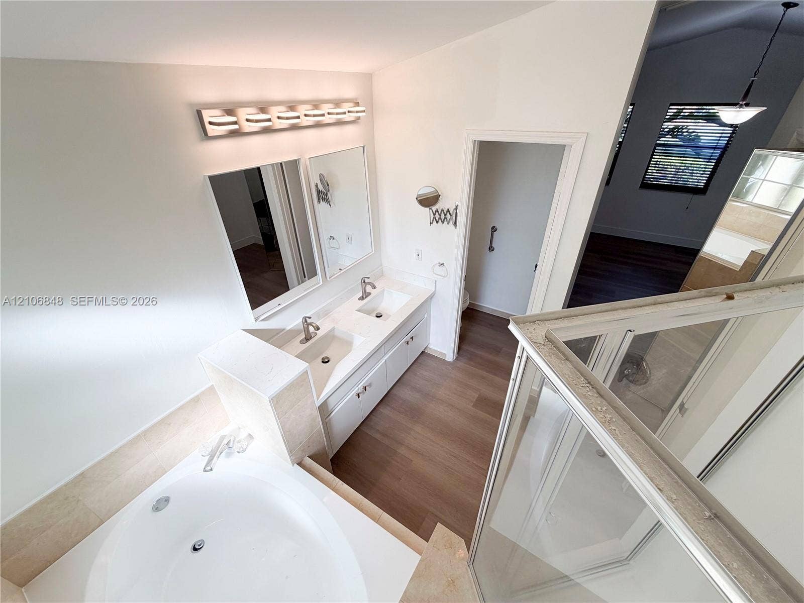 Dual-sink vanity with white cabinetry and quartz countertop, large soaking tub, wood-finish flooring, and glass-enclosed shower