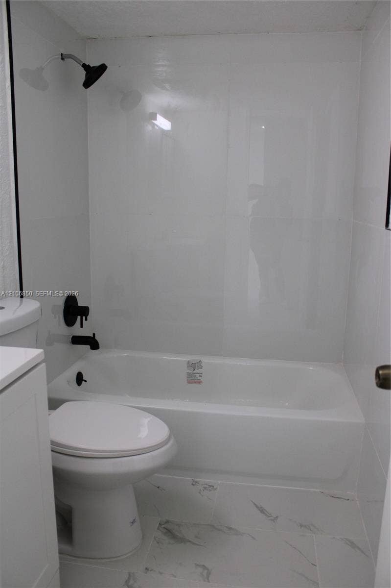 Bathroom featuring a porcelain tub with high-gloss wall surround, matte black rainfall showerhead, matching matte black plumbing fixtures, and patterned tile flooring