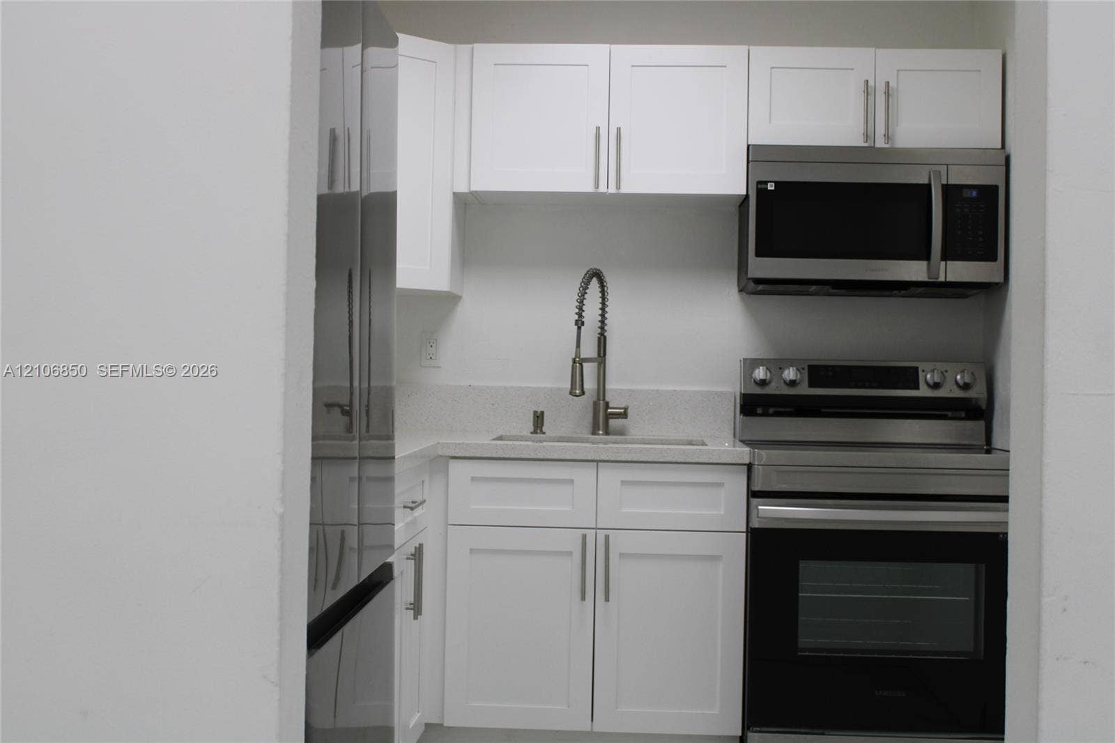 Kitchenette featuring white Shaker-style cabinetry, stainless steel appliances, a stone-composite countertop, and a gooseneck faucet