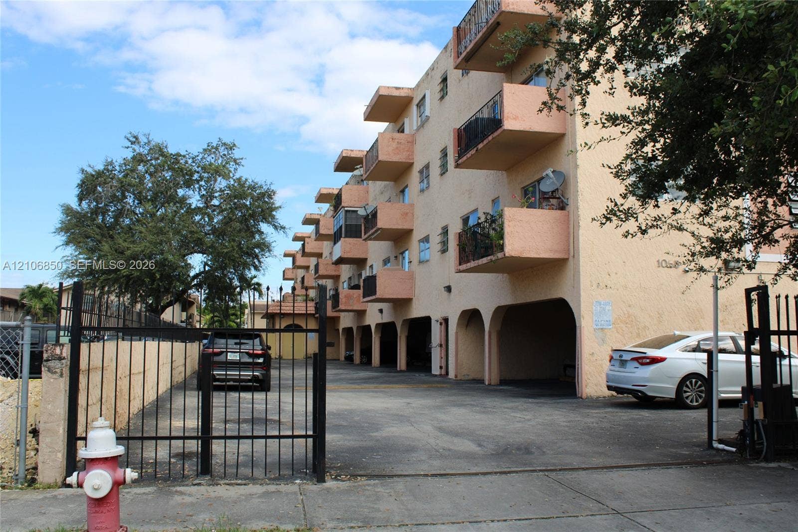 Multi-story stucco exterior featuring private cantilevered balconies, arched ground-level covered parking, and metal perimeter fencing