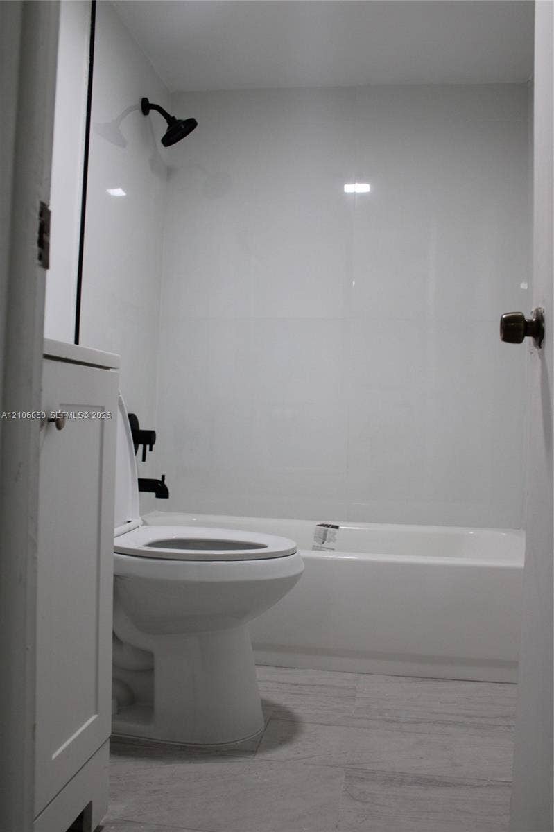 Full bathroom featuring a white bathtub, smooth wall panels, matte black shower head and hardware, and wood-finish flooring