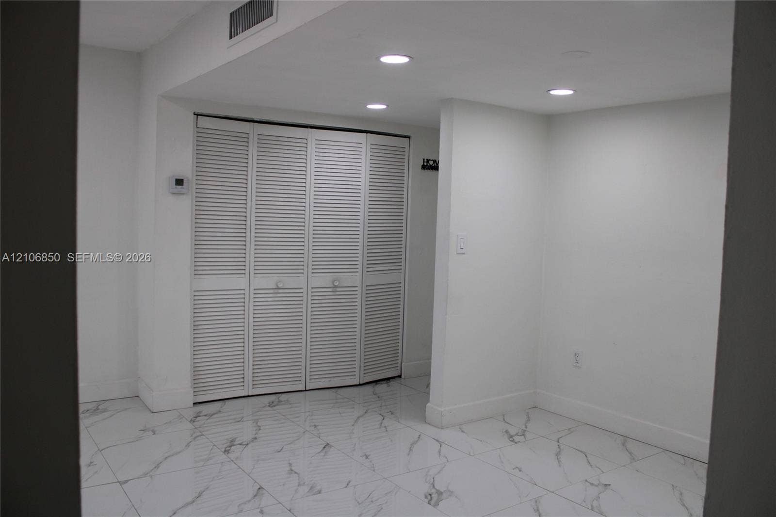 Interior space featuring white stone-finish flooring with grey veining, four-panel louvered closet doors, and recessed ceiling lighting