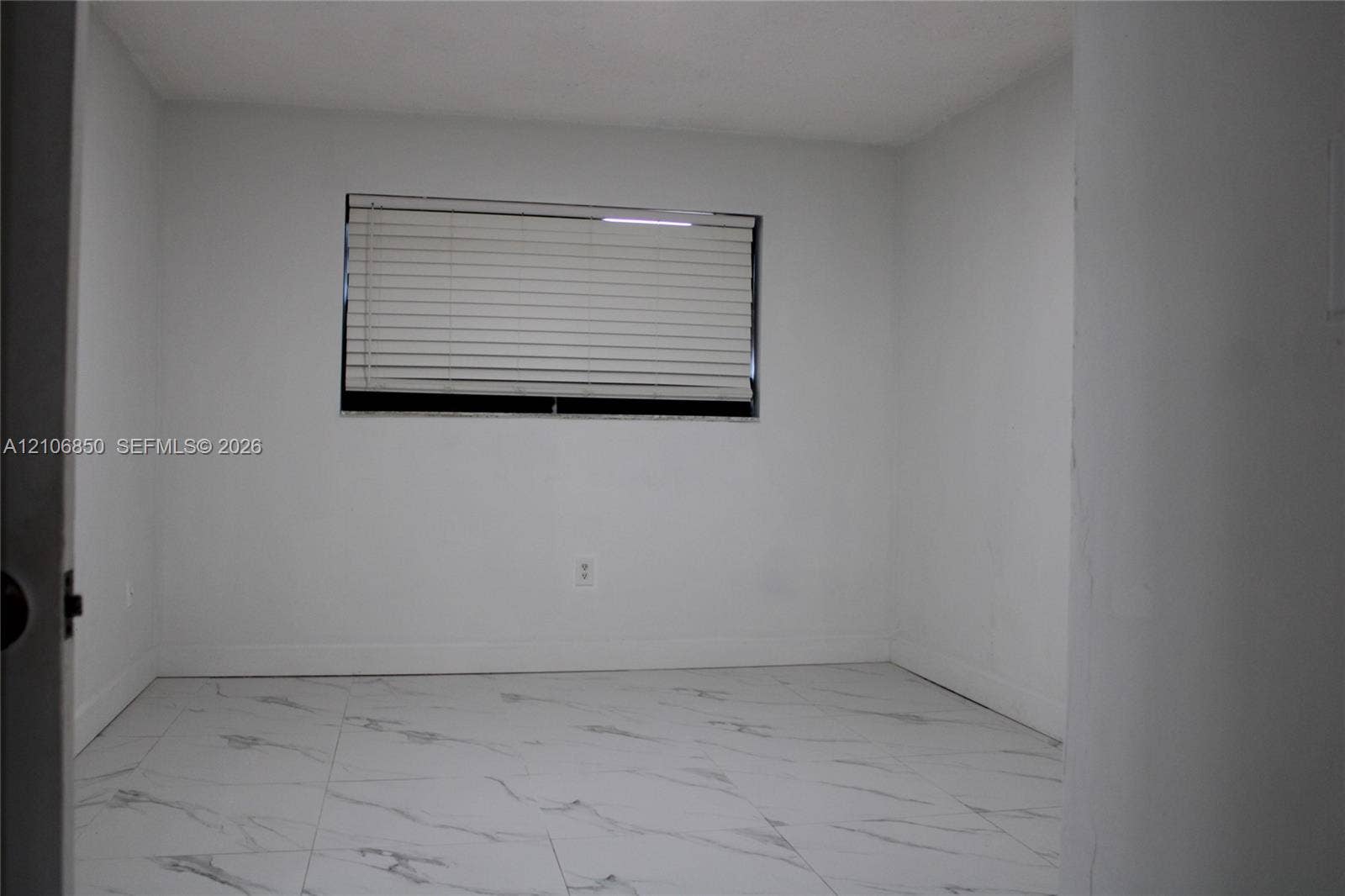 Interior room featuring large-format, white veined tile flooring, neutral wall finishes, and a window with horizontal blinds