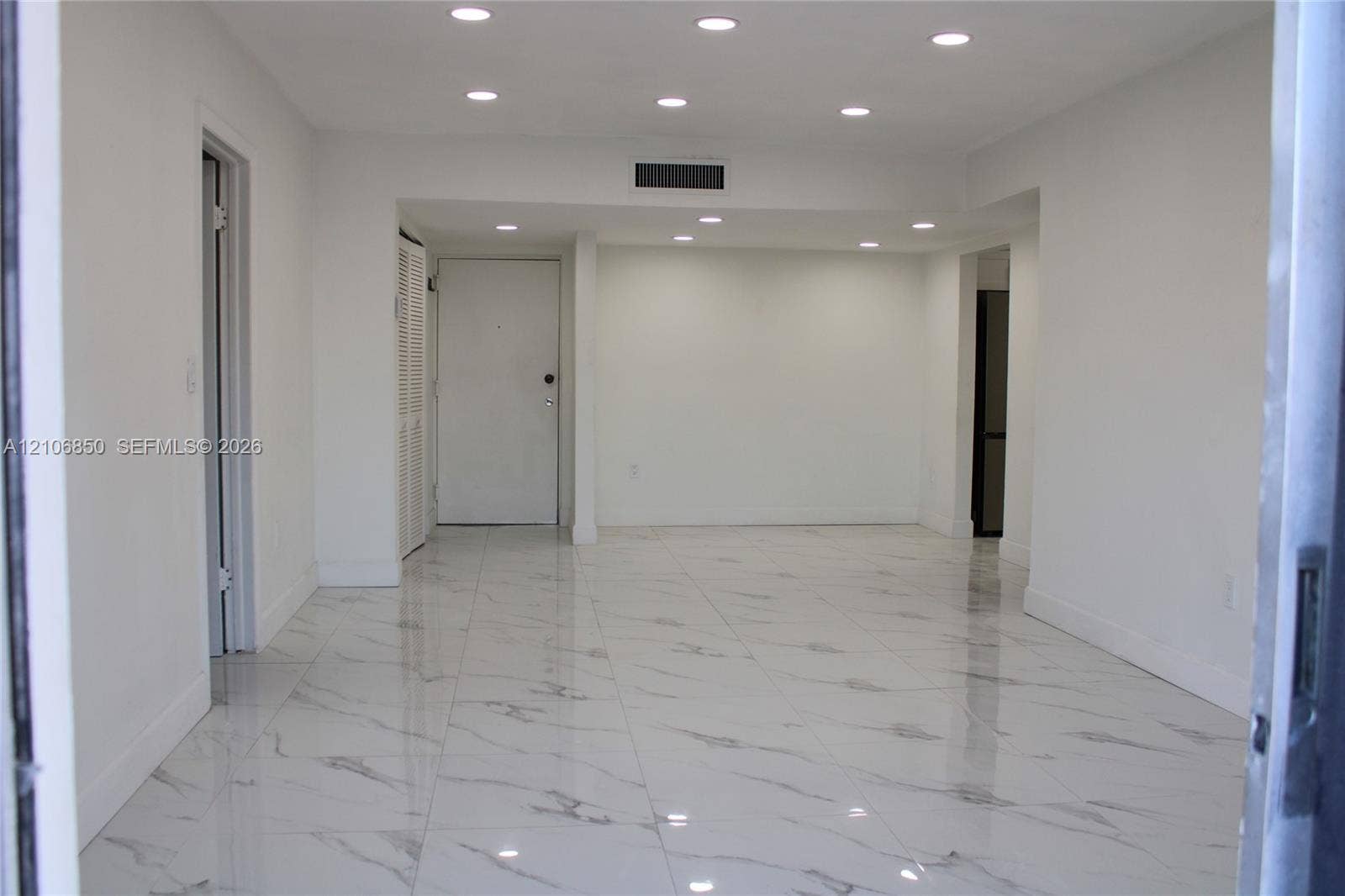 Interior space featuring high-gloss, large-format veined tile flooring, crisp white walls, and recessed ceiling lighting