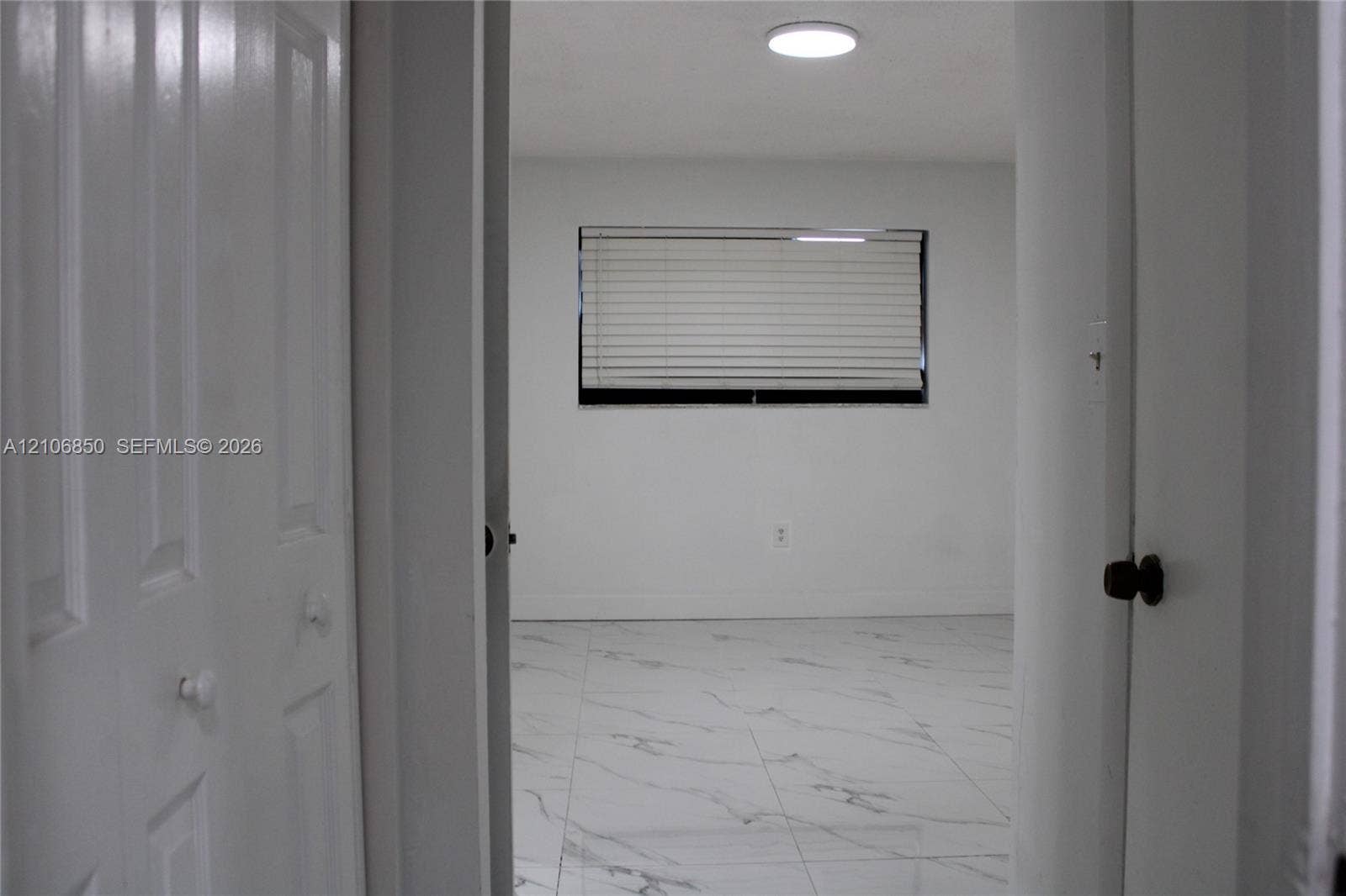 Interior room featuring large-format light-toned tile flooring with veining, multi-panel closet doors, and a window with horizontal blinds